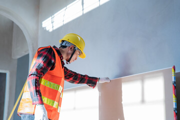 A craftsman wearing a yellow hard hat is inspecting building materials.