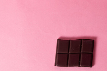 Perfect chunk of dark chocolate on the side. Pink background. Copyspace.
