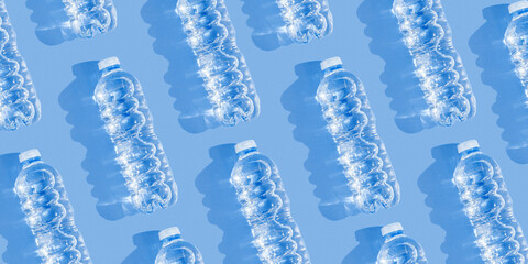 Pattern small plastic bottles with clean drinking water at sunlight, shadow on blue background,...