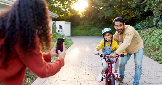 Happy family, parents and teaching kid on bicycle with phone to record video, photograph and childhood growth. Mom, dad and memory of girl learning to ride bike with support, play and development