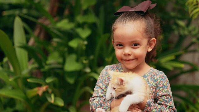 Niña latina feliz jugando con su mascota un pequeño gatito gato felino travieso e inquieto en el jardín al exterior al aire libre 