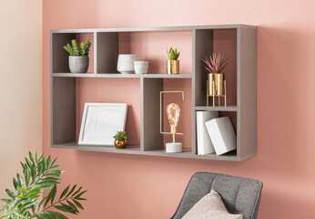 A grey shelf with multiple green potted plants on it, standing against a wall and next to a white...