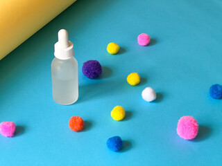 Serum in a glass bottle on a blue background with a multicoloured pom-pons