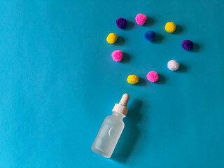 Serum in a glass bottle on a blue background with a multicoloured balloons folded in the shape of a heart