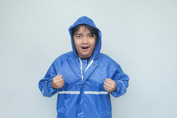 Asian young man with happy expression in blue raincoat on gray background.