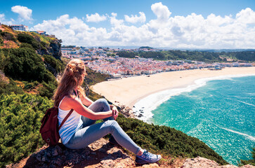 Fototapeta na wymiar Woman sitting on cliff enjoying panoramic view of the beach- Nazare in Portugal