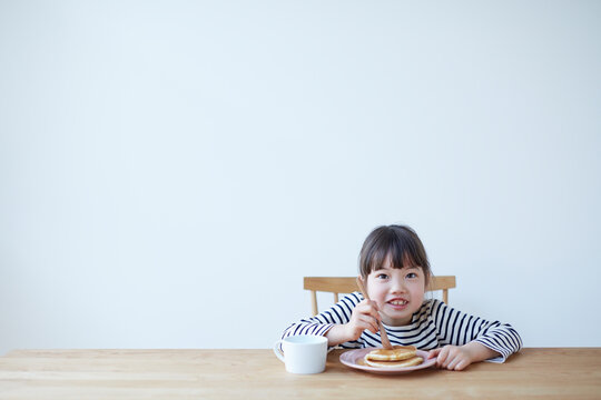 テーブルでホットケーキを食べる女の子