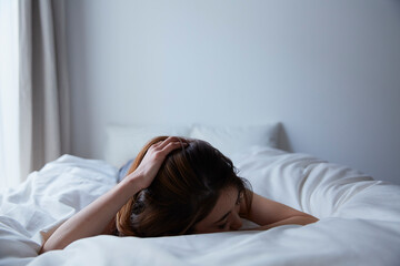 ベットの上でうつ伏せになって頭を抱える女性