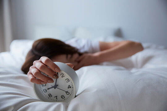 ベットの上で目覚まし時計を握ってあくびをする女性