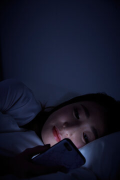 暗闇の中ベットに寝転んでスマートフォンを見る女性