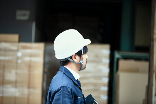 倉庫の前に立つ後ろ姿のヘルメットの男性
