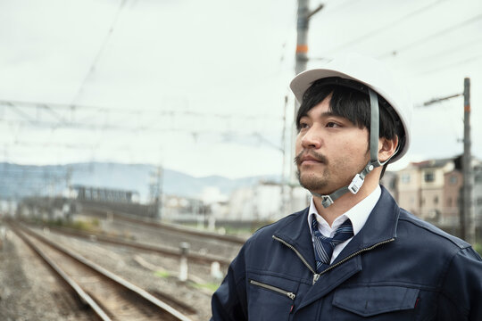線路をバックに立つ作業服とヘルメットの男性