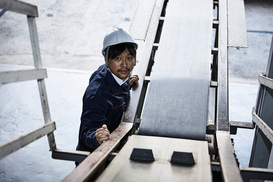 ベルトコンベアーを見上げている作業服とヘルメットの男性