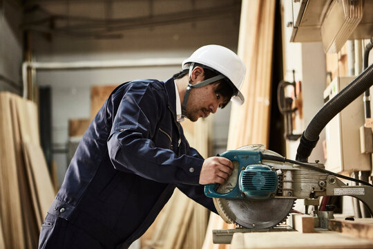 電動のこぎりを使う作業服とヘルメットの男性