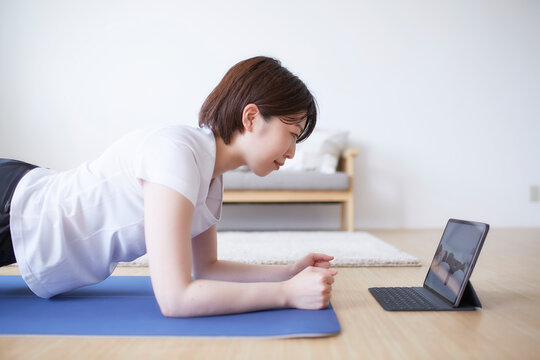 室内の床でノートパソコンを見ながらトレーニングする女性