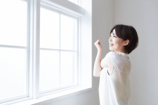 窓へで外を見ながら腕のストレッチをする女性