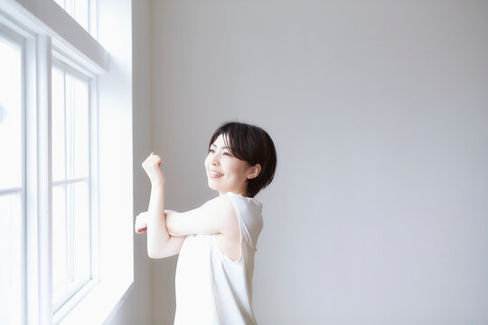 窓へで外を見ながら腕のストレッチをする女性
