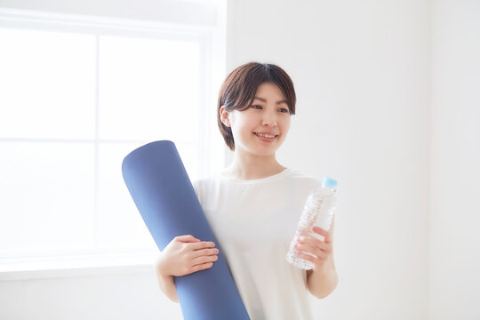 室内でヨガマットとペットボトルを手に持つ女性