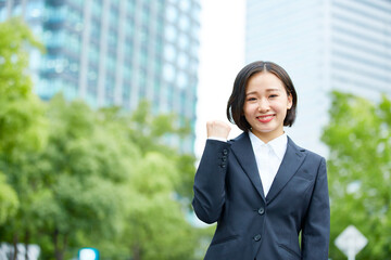 ビル の背景とリクルートスーツを着たガッツポーズの笑顔の女性