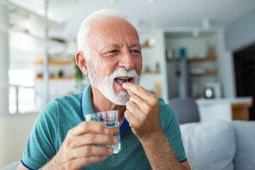 Senior man takes pill with glass of water in hand. Stressed mature man drinking sedated...