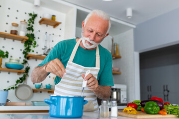 Happy senior man having fun cooking at home - Elderly person preparing health lunch in modern kitchen - Retired lifestyle time and food nutrition concept