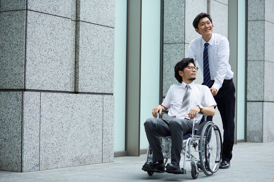 オフィス街で車椅子の男性を押しているスーツの男性