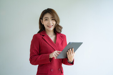 Beautiful Asian businesswoman in a red suit standing and holding a digital tablet over white background.