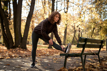 Full length of ginger woman stretching on bench before jogging in the park