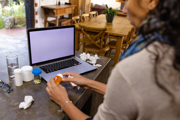 Biracial woman sitting at countertop, using laptop with copy space for medical consultation