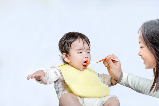 お姉さんから離乳食を食べさせてもらう赤ちゃん。育児、子育て、愛情イメージ