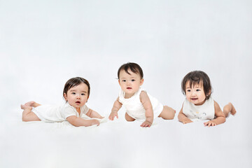 白背景の前でハイハイする3人の赤ちゃん