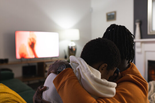 African american couple relaxing at home, scared, hugging, watching scary movie