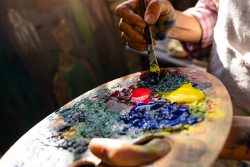 Close up of biracial woman painting on easel using brush and colour palette in garden
