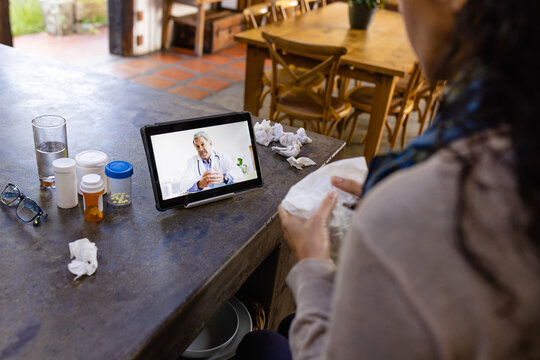 Biracial woman sitting at countertop, using tablet for medical consultation with biracial doctor