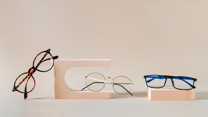 Glasses sale banner. Optic store sale-out offer. Trendy glasses in plastic and metallic frame on podiums on beige background. Eyewear collection. Copy space for text. Optic store discount. Minimalism