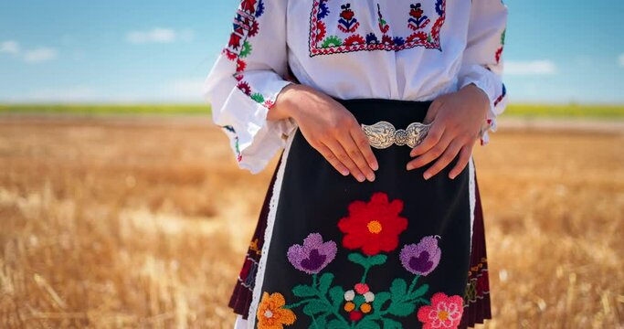 Girl in traditional ethnic folklore costume with Bulgarian embroidery and silver belt buckle standing on a harvest golden wheat field