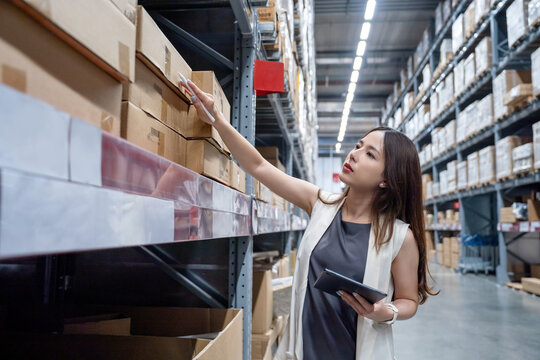Young smart asian business working woman using digital tablet to check goods on shelves for product management in warehouse, Logistics business planning concept.