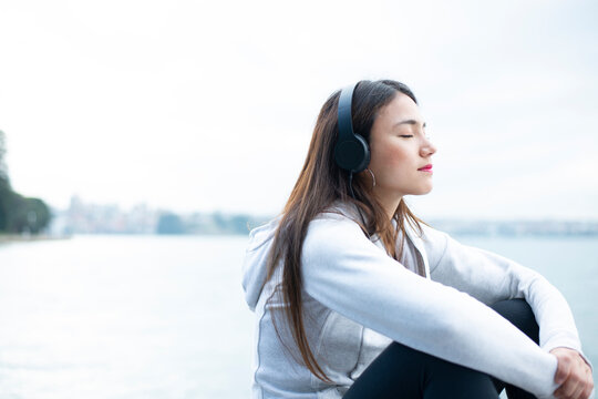 水辺で目をつぶって音楽を聴いている女性