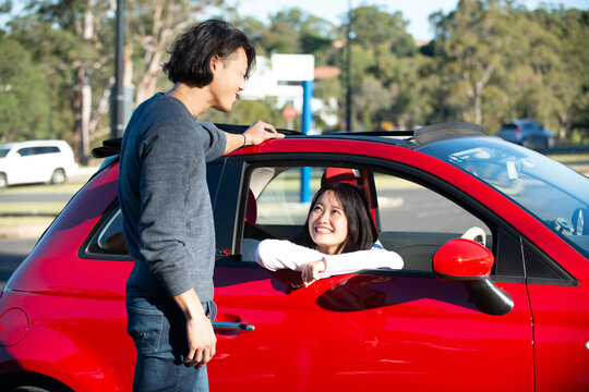 赤い車の前で話している男女