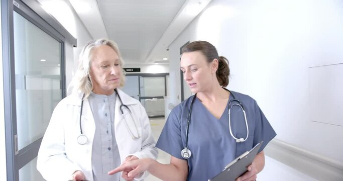 Caucasian female doctors in discussion using tablet in hospital corridor, slow motion