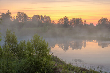 Clouds of mist float over the river on a cool summer morning at dawn.