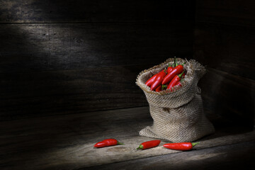 Still life, hessian bag full of red chilli peppers, rustic wooden box, pools of soft, dark, mood...