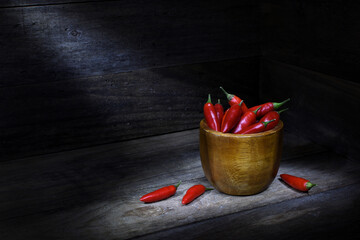 Still life, brown, wooden bowl full of red chilli peppers, rustic wooden box, pools of dark, mood lighting, copy space to the left