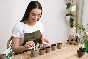 Woman inserting cards with names of vegetable seeds into peat pots at table indoors