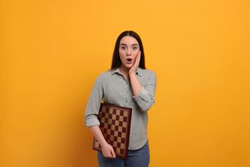 Emotional woman with chessboard on orange background