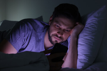 Fototapeta na wymiar Man using smartphone in bed at night. Internet addiction