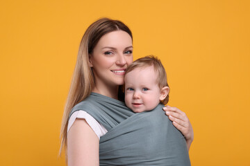 Mother holding her child in baby wrap on orange background