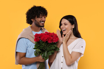 International dating. Handsome man presenting roses to his beloved woman on yellow background