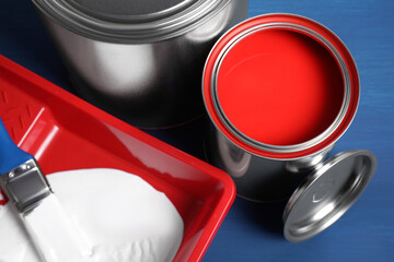 Cans of paints, brush and tray on blue wooden background, closeup