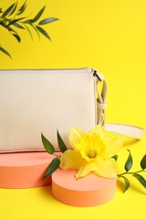 Stylish presentation of bag, green leaves and daffodil flower on yellow background